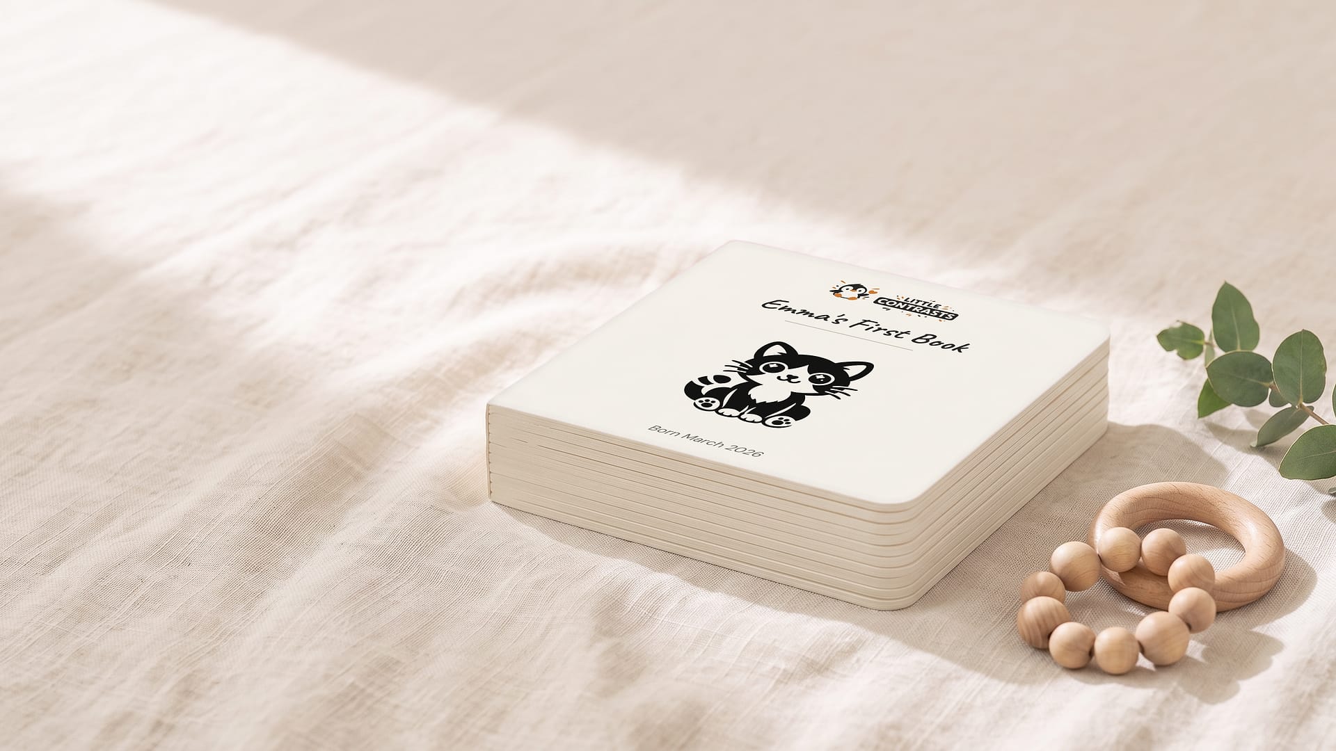 Illustrative mockup: Emma's personalised board book, closed, on linen beside a wooden rattle